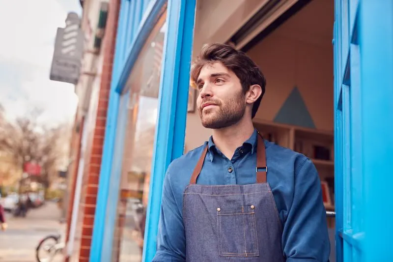 Small business owner standing at the front of a local shop, ready to welcome customers.