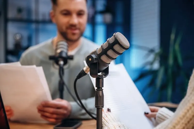 Podcasters recording an episode with microphones and notes in a studio.
